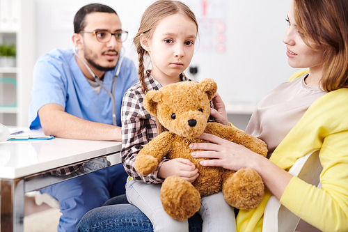 portrait of young middle-. doctor listening to little girl breathing using stethoscope during consultation in modern clinic