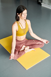High angle portrait of contemporary woman doing yoga sitting in lotus position on floor and meditating to music
