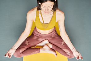 Above view portrait of contemporary woman doing yoga sitting in lotus poition on floor and meditating to music