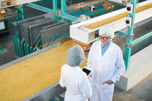 High angle portrait of senior factory manager talking to young worker during quality inspection  in food production workshop, copy space