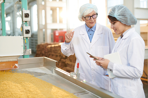 Waist up portrait of senior factory manager talking to young worker during quality inspection  in food production workshop, copy space