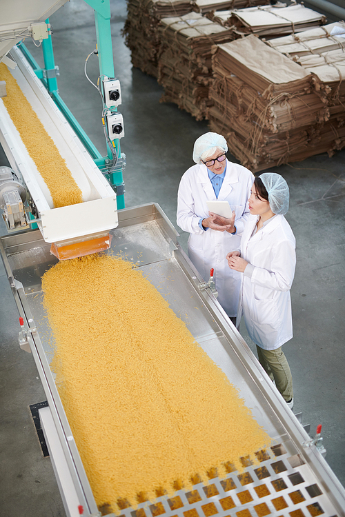 Above view portrait of two factory workers standing by conveyor belt during quality inspection at food production, copy space