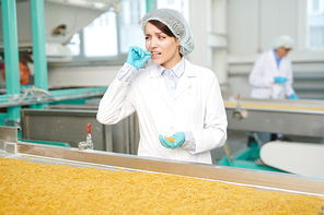 Portrait of pretty young woman working at modern food factory, tasting dry macaroni on production line, copy space