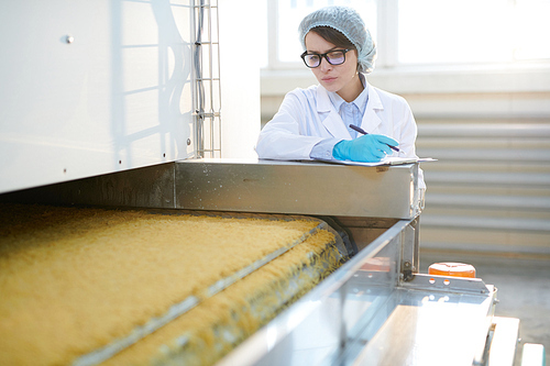 Portrait of  young woman working at factory and inspecting food production standing by macaroni conveyor belt, copy space