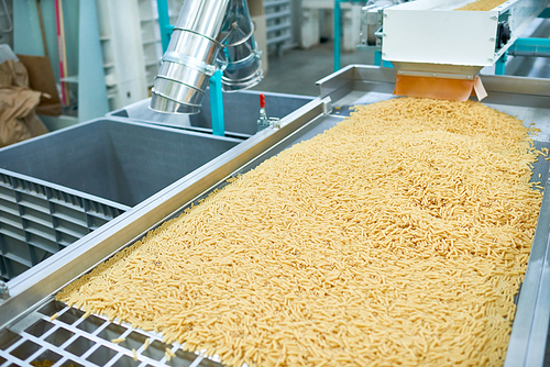 Crop shot of production process at modern food factory, focus on macaroni ready for packaging sliding down assembly line, copy space