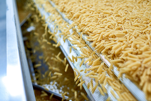 Close up of dry macaroni spilling from machine unit on modern food production factory, copy space