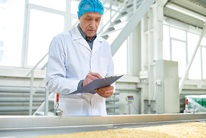 Waist up portrait of senior factory worker  in food industry holding clipboard standing by conveyor belt, copy space