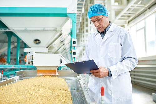 Portrait of senior factory worker  holding clipboard standing by conveyor belt in modern production workshop, copy space