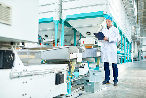 Full length portrait of senior factory worker  holding clipboard standing in clean production workshop, copy space