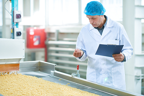 Portrait of senior factory worker checking production process at food plant standing by conveyor belt in modern clean workshop, copy space