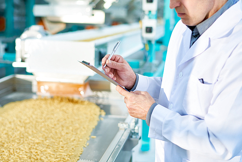 Mid section portrait  of  unrecognizable factory worker doing  production quality inspection in food industry holding clipboard and standing by conveyor belt, copy space