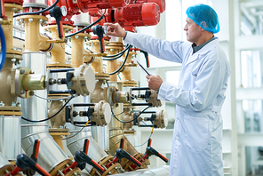 Side view portrait  of senior factory worker doing  production quality inspection in checking pipes and valves in modern workshop, copy space