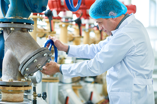 Side view portrait  of senior factory worker doing  production quality inspection and  checking pipes and valves in modern workshop