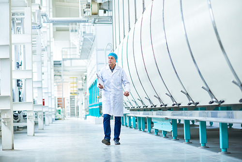 Full length portrait of senior factory worker walking towards camera crossing workshop of modern plant, copy space