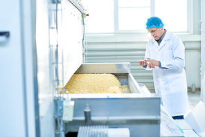 Portrait of senior factory worker doing  quality inspection in food plant standing by machine unit with macaroni, copy space