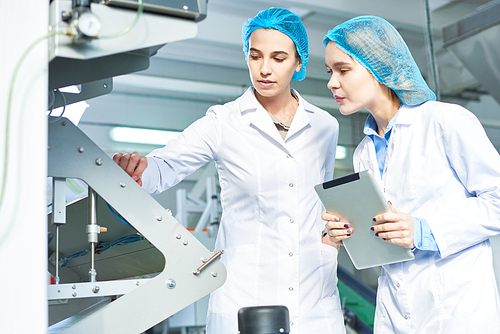 Portrait of two young women  wearing lab coats working at modern food factory and smiling while checking production process standing by power units in workshop, copy space