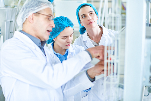 Portrait of two young women listening to senior factory worker during training seminar for new specialists standing in clean workshop of modern plant