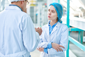 Portrait of young woman listening to senior mentor while working in clean production workshop of modern plant