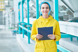 Waist up portrait of cheerful young woman  standing in clean production workshop of modern plant and holding clipboard, copy space