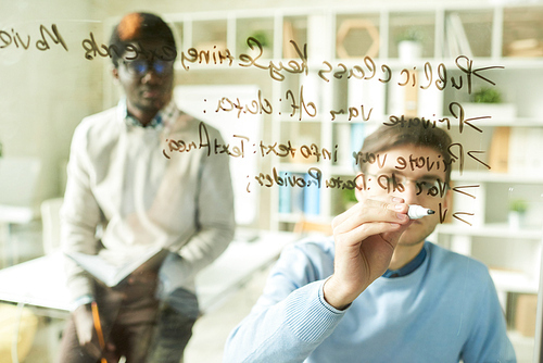 Portrait of two IT specialists writing formulas on glass wall in modern office, focus on foreground, copy space