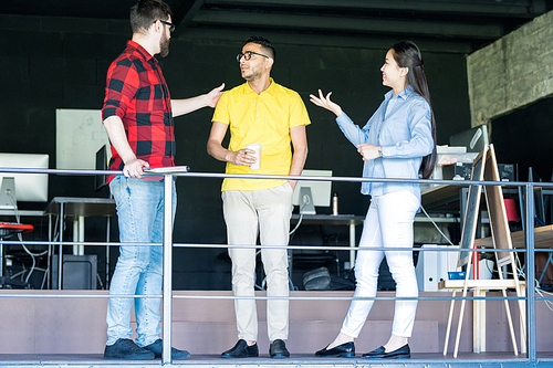 Full length portrait of three creative young people wearing colorful clothes chatting during break standing on balcony in modern office