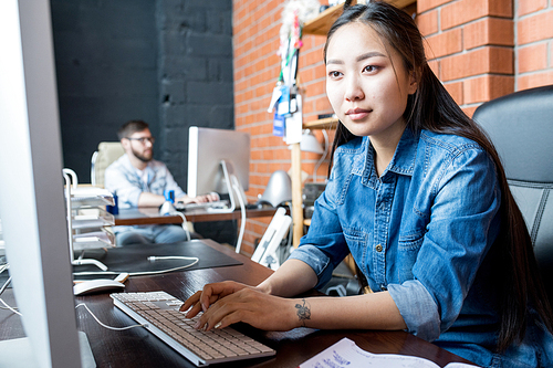 Portrait of young Asian woman wearing casual clothes using PC sitting at desk in modern office