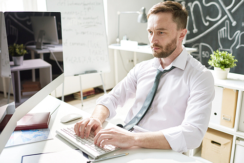 Portrait of handsome bearded businessman sitting at desk in office and using modern computer, typing, copy space