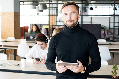Waist up portrait of handsome contemporary businessman  and holding digital tablet while posing in open space office of startup company, copy space