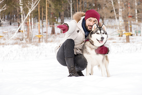 Full length portrait of modern Asian man lovingly talking to gorgeous Husky dog while enjoying time outdoors in winter, copy space