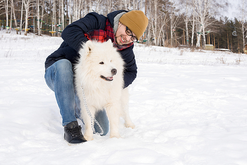 Full length portrait of modern adult man petting white Samoyed dog outdoors on nice winter day, copy space