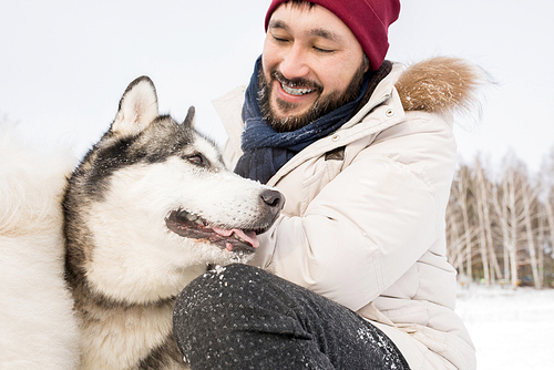 Portrait of cheerful Asian man petting gorgeous Husky dog enjoying walk outdoors on winter day