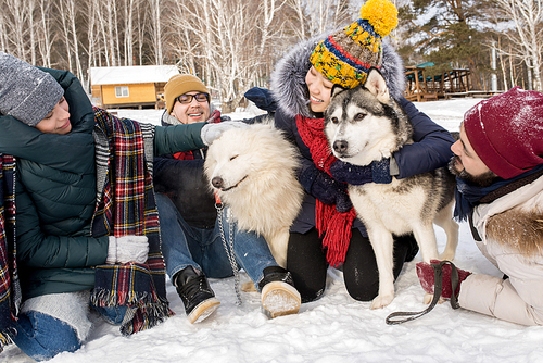 Full length portrait of  happy young people playing with two dogs outdoors in snow while enjoying time in winter resort