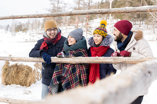 Portrait of four young people leaning on wooden fence enjoying winter vacation together, copy space