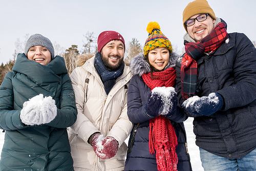 Waist up portrait of four young friends having fun outdoors on winter day holding handfuls of snow playing snowball fight