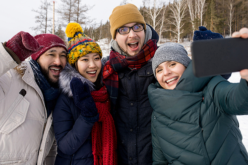 Waist up portrait of four happy young people taking selfie photo while having fun outdoors in winter