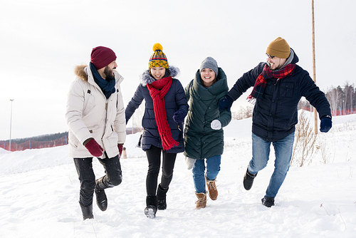 Portrait of four young people running towards camera having fun enjoying nice winter days outdoors, copy space