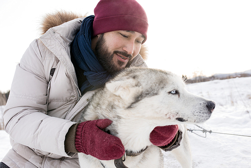 Portrait of bearded Asian man hugging gorgeous husky dog enjoying nice winter day on walk in the woods, copy space