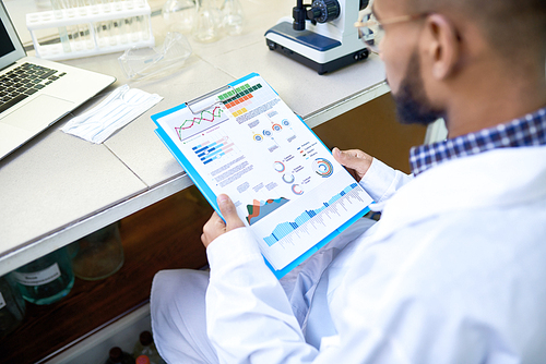 Over shoulder portrait of young Middle-Eastern scientist looking at data charts while working on medical research in laboratory