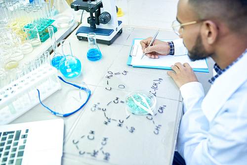 High angle portrait of young Middle-Eastern scientist studying chemical structures in modern medical laboratory, copy space