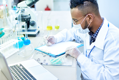 Side view portrait of young Middle-Eastern scientist working with petri dish studying chemical structures in modern medical laboratory