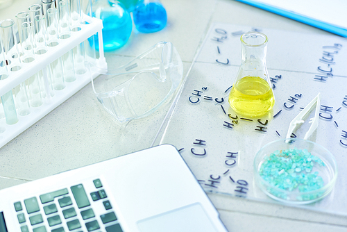 Close up background of working desk in modern science laboratory: test tubes, chemical formulas and laptop on table