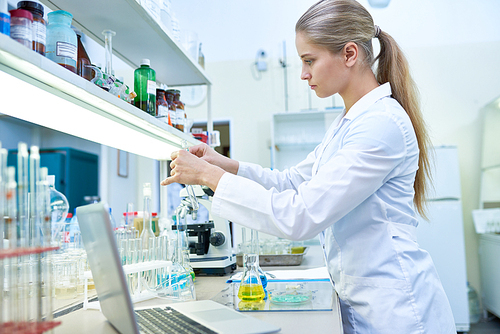 Side view portrait of pretty female scientist  working with test tubes studying chemicals in medical laboratory, copy space