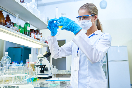 Portrait of pretty female scientist wearing protective mask working with test tubes studying chemicals in medical laboratory, copy space