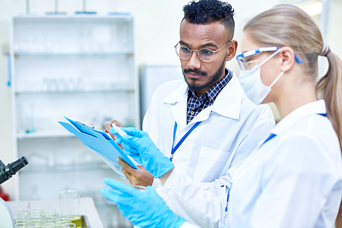 Portrait of two young scientists, one of them Middle-Eastern, working together in medical laboratory doing research on  medical drugs, copy space