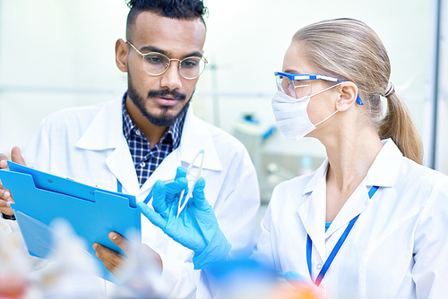 Portrait of two young scientists, one of them Middle-Eastern, working together in medical laboratory doing research on  chemicals and bacteria