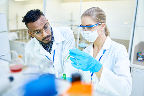 Portrait of two young scientists, one of them Middle-Eastern, working together in research laboratory testing chemicals and bacteria