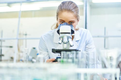 Portrait of young female scientist looking in microscope while working on medical research in science laboratory, copy space