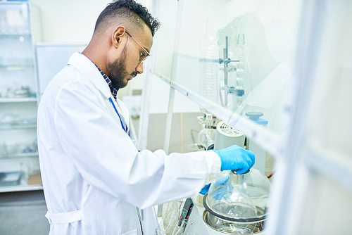 Side view portrait of young Middle-eastern scientist working with sanitizing equipment in medical research laboratory, copy space