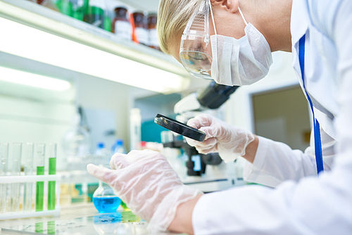 Side view portrait of young female scientist looking at test results with magnifying glass while working in medical laboratory doing drug research, copy space