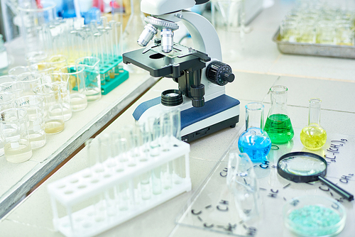 High angle of various scientific equipment on working table in research laboratory, modern microscope surrounded by test tubes and glassware